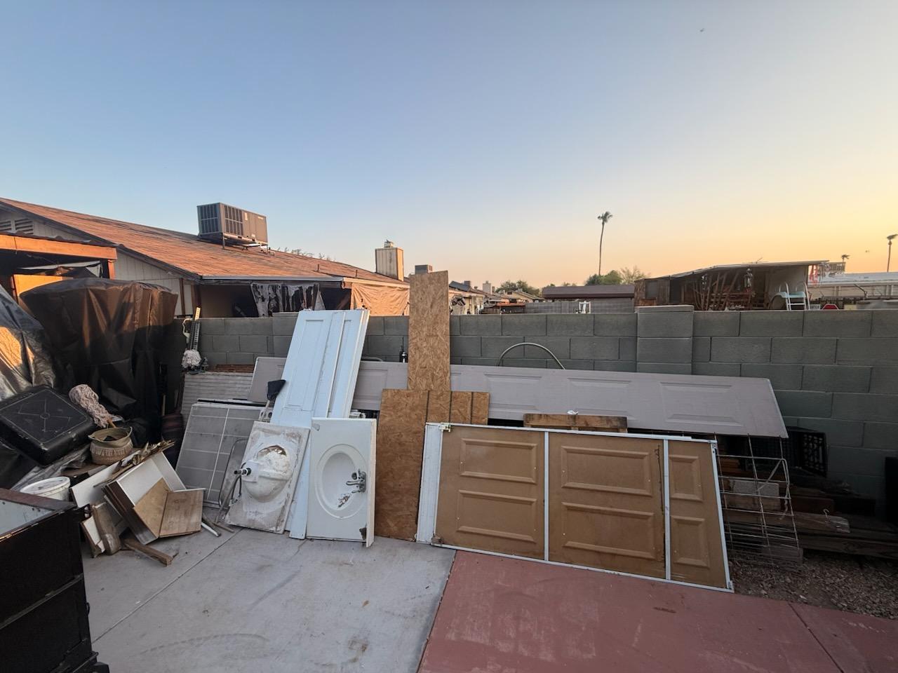 Backyard patio stacked with old doors, cabinets, a sink, plywood, and construction debris before removal